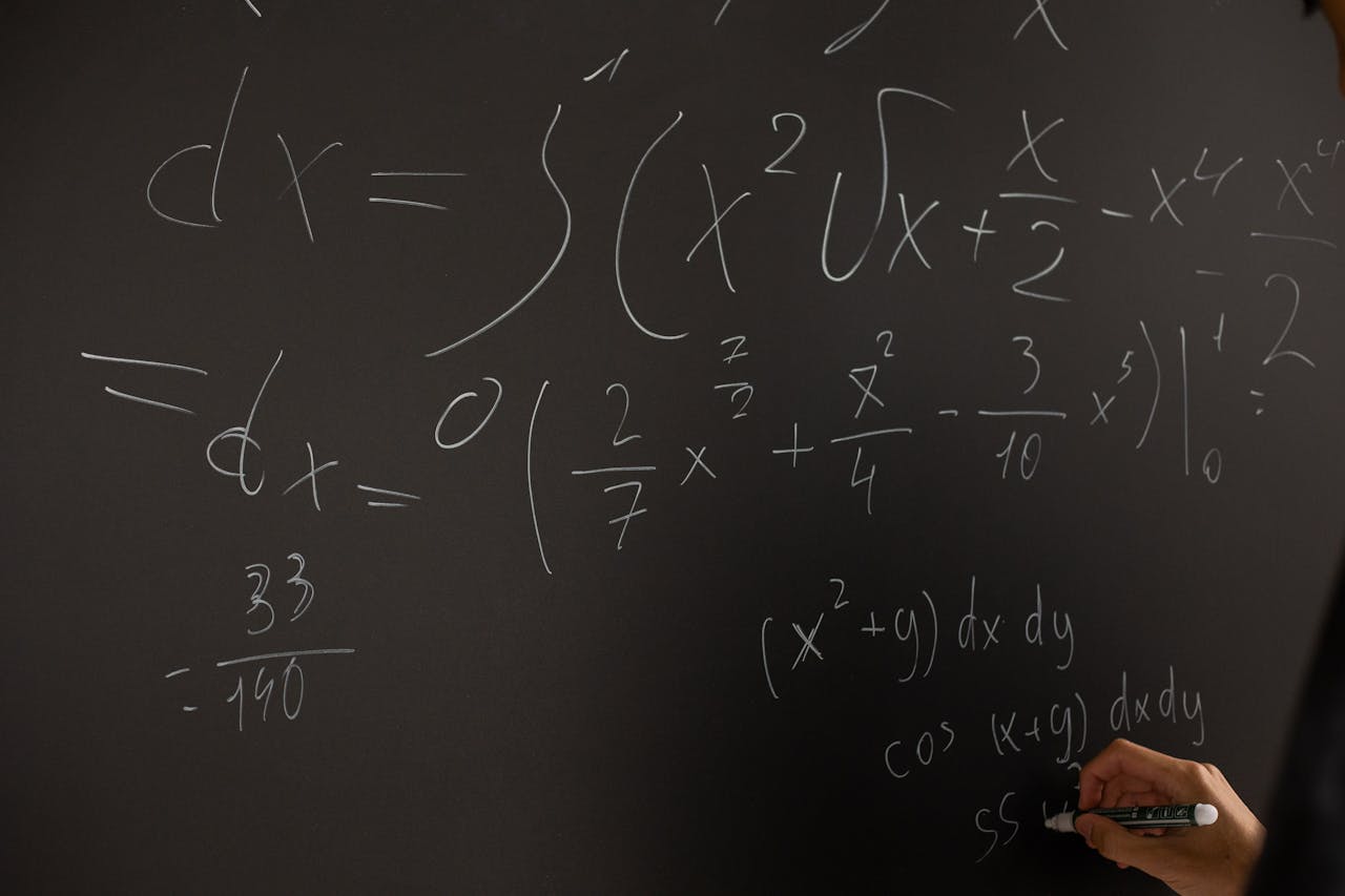 Close-up of hand writing complex math equations on a chalkboard in a classroom setting.